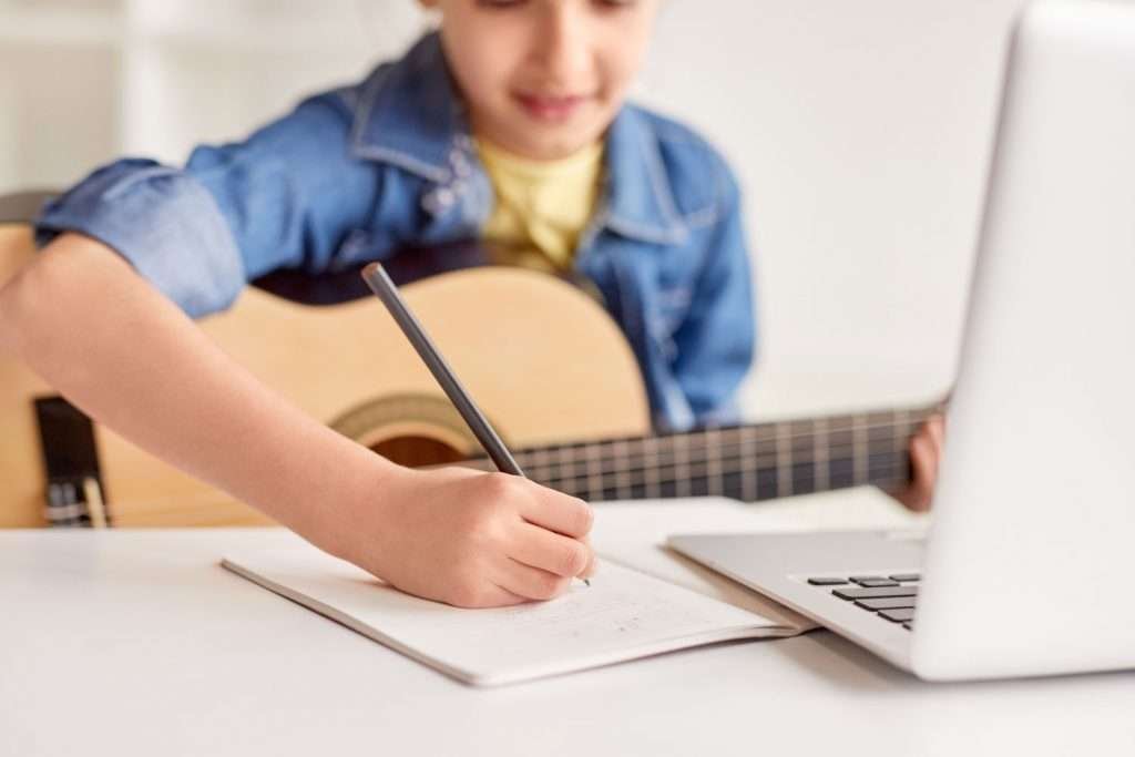 Boy holding a guitar and writing with a pencil in his notebook
