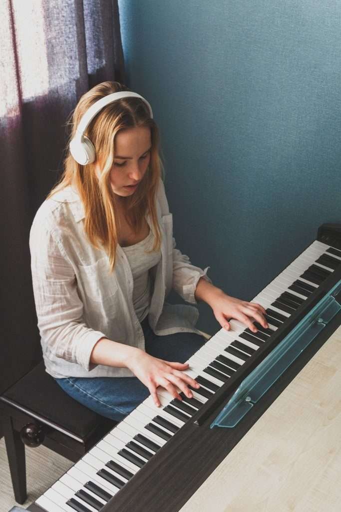 teenage girl playing the piano while wearing headphones